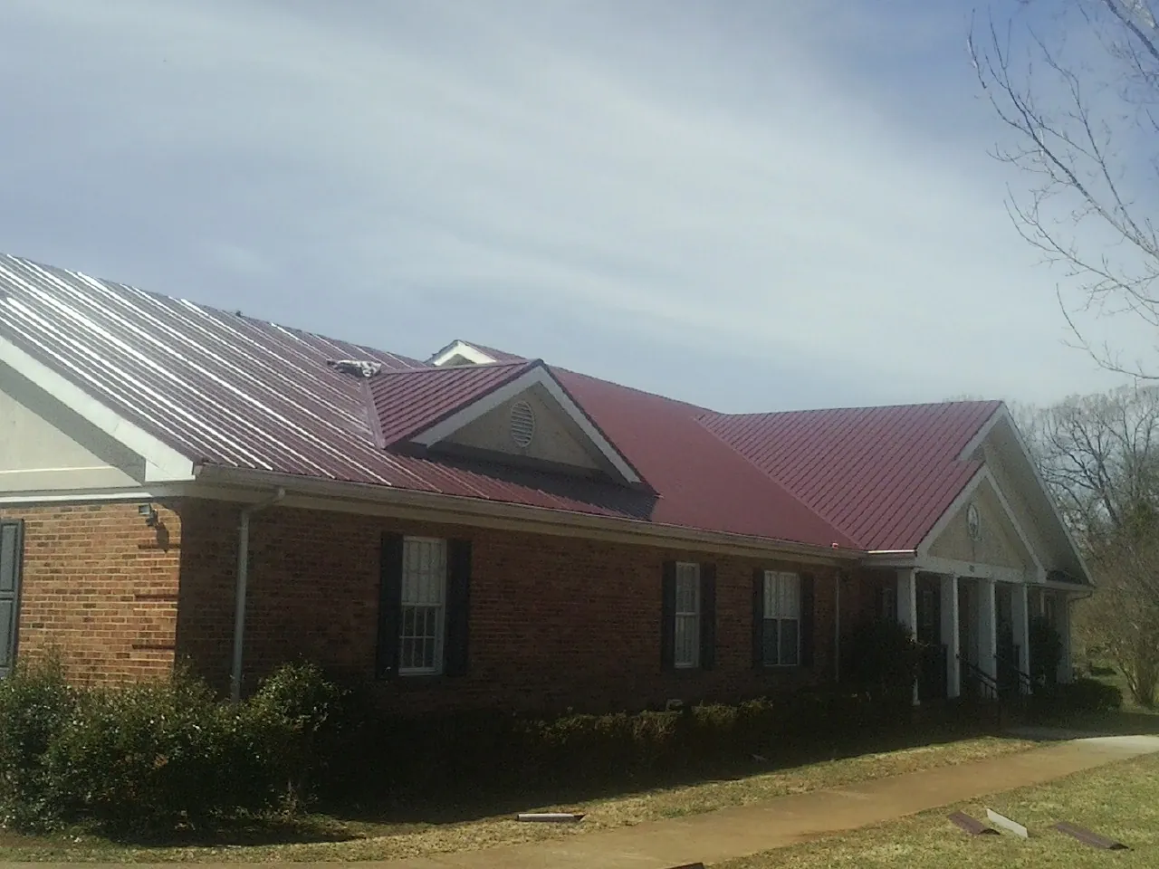 Red metal roof with gabled entries on a long brick building, from a Hail Damage Roof Repair job in Hanson