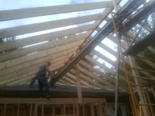 Rafters going up over a new addition with a worker on the wall in Hanson