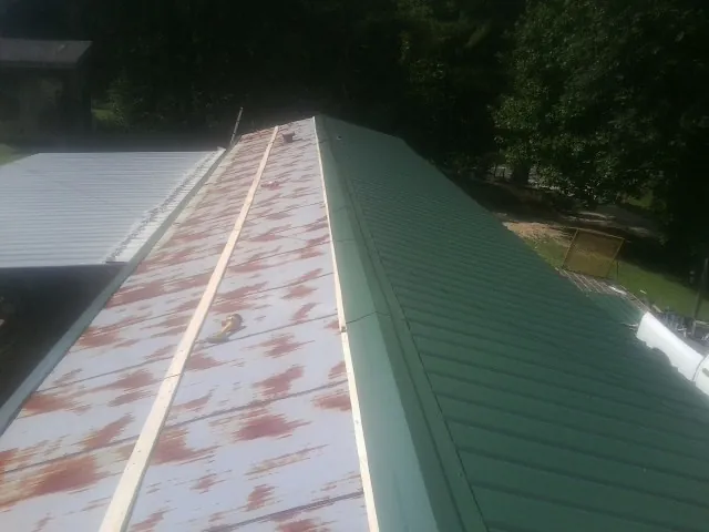 Old rusted panels beside newly installed green metal roofing — Wind Damage Roof Repair by Roofing Brothers in Hanson