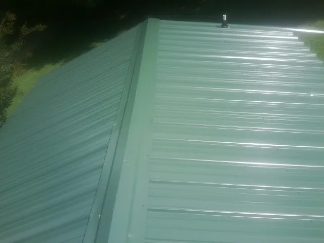New green metal panels meeting at the ridge of a roof — Flat Roof Repair work by our crew in Hanson