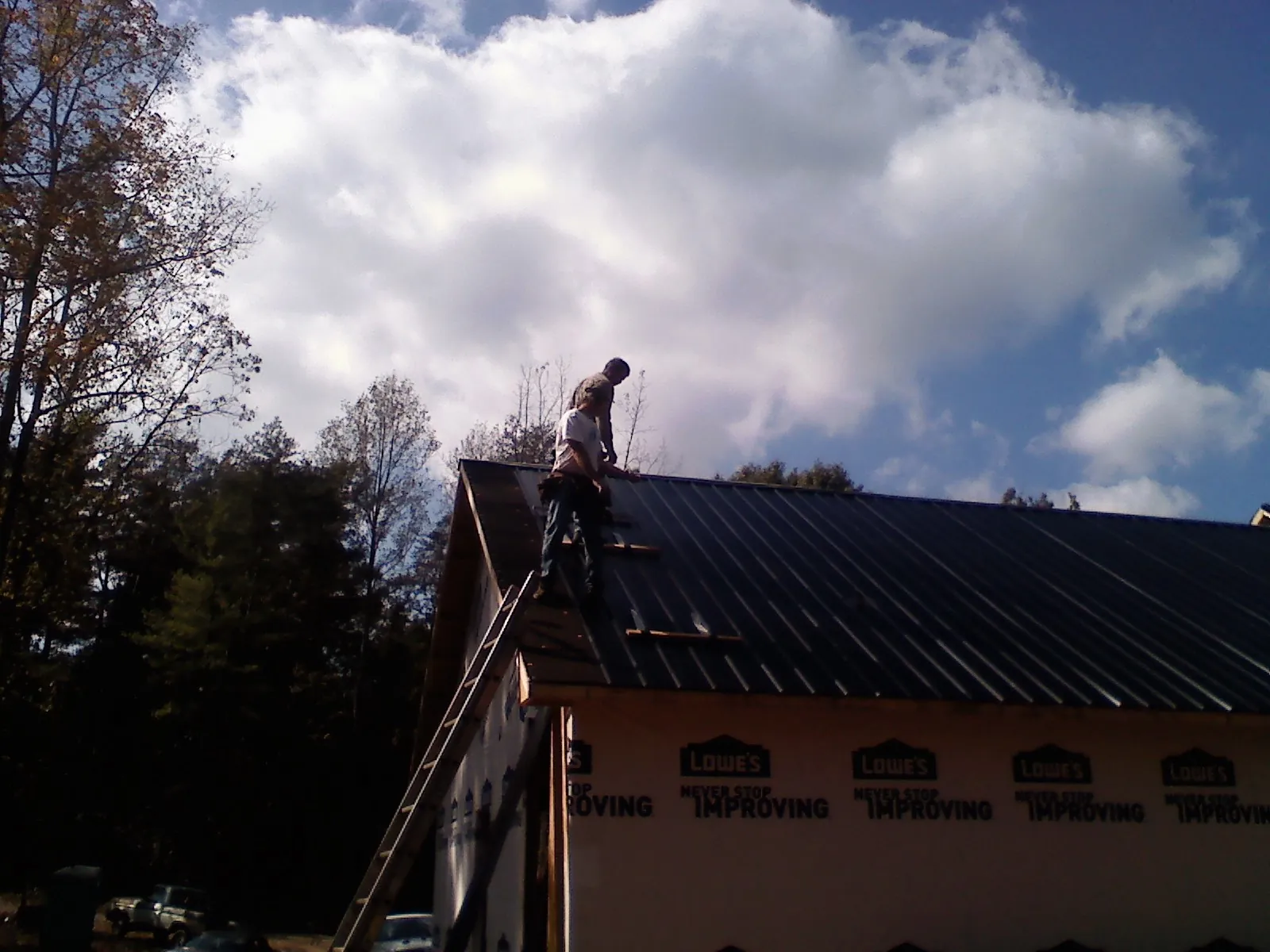 Roofer fastening dark metal panels high against a cloudy sky, from a Roof Inspection job in Hanson