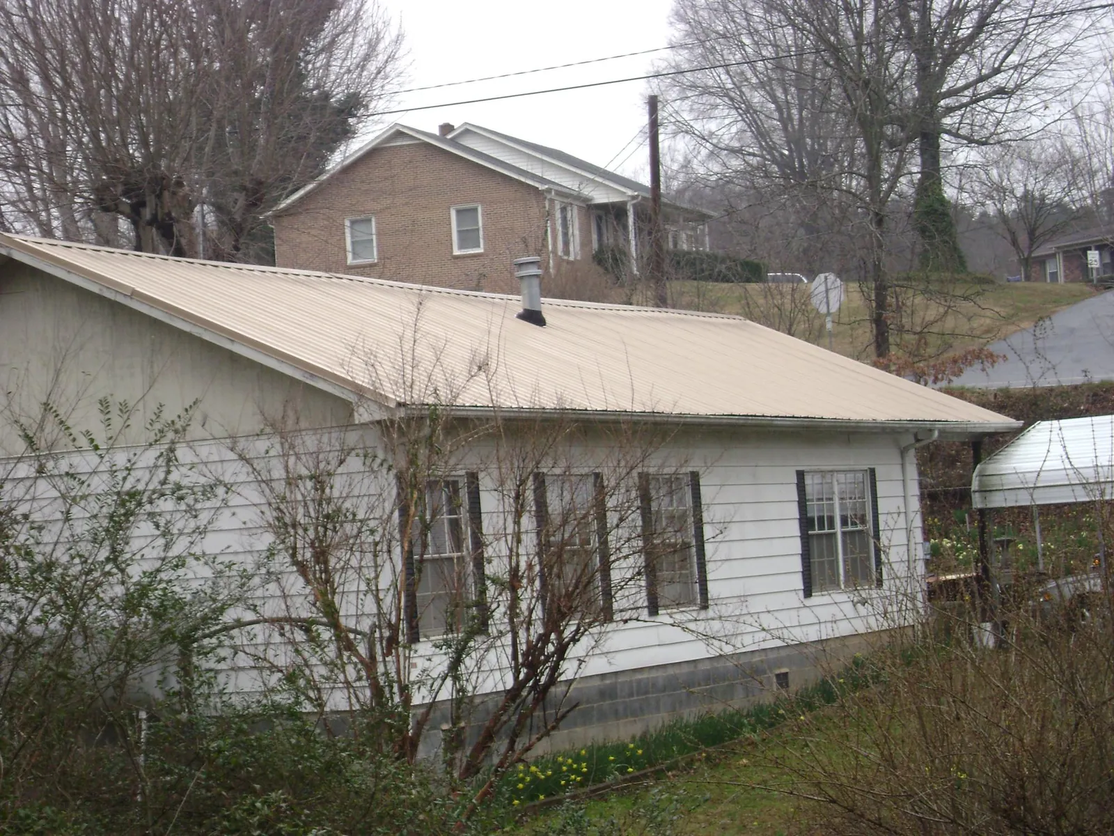 Tan metal roof on a white sided house set into a hillside — Commercial Roofing by Roofing Brothers in Hanson