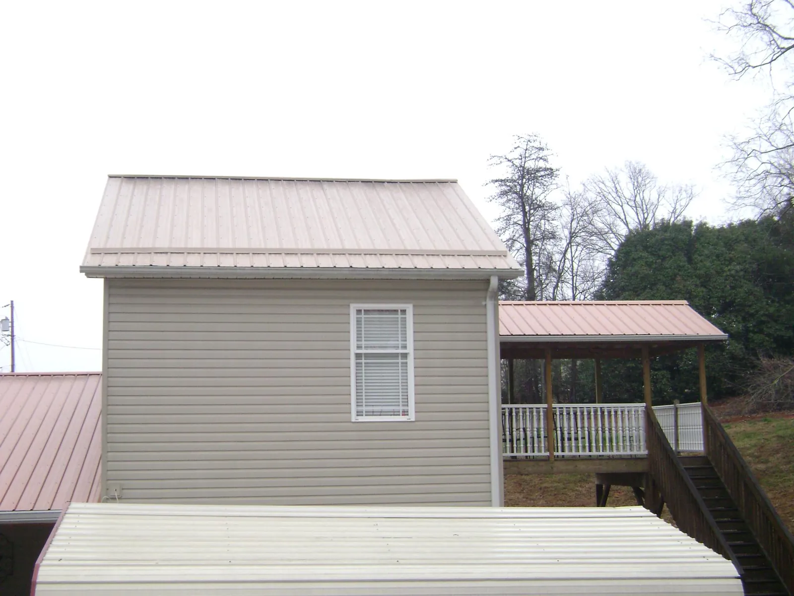 Tan metal roofs on a two story addition and attached porch, from a Roof Replacement job in Hanson